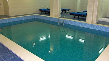 Una piscina interior con agua cristalina, borde de azulejos y zona de duchas.