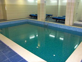 An indoor swimming pool with clear water, a tiled edge, and a shower area.