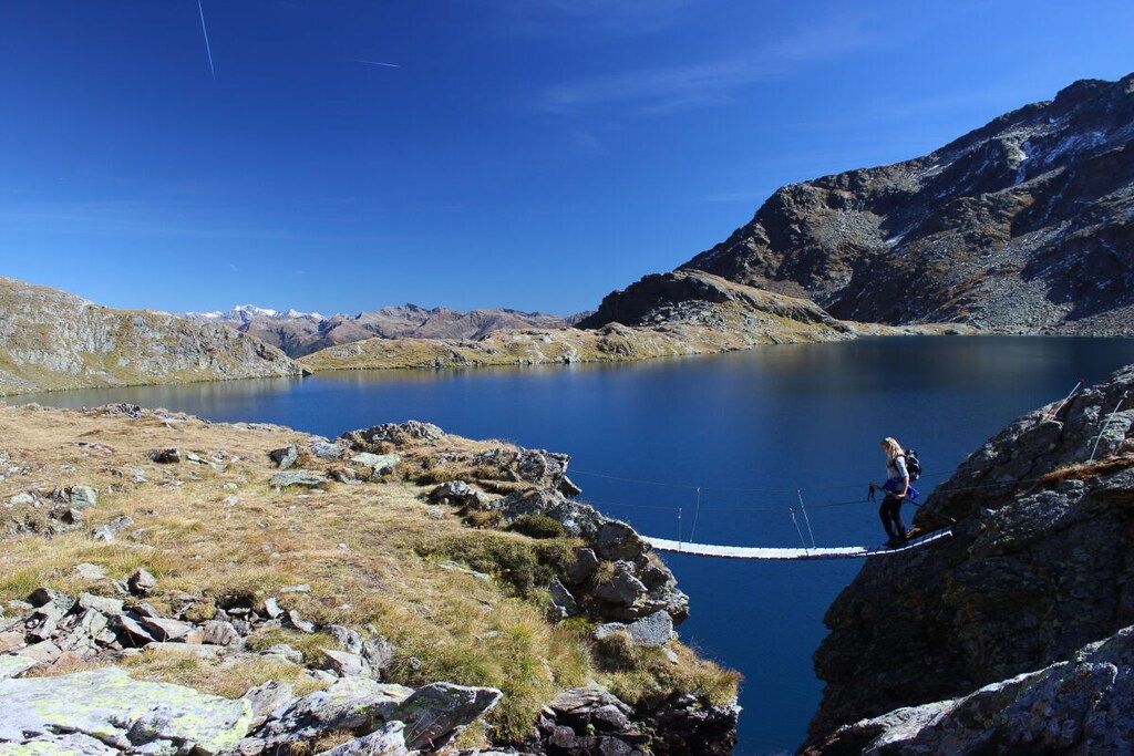 Een natuurlandschap met een meer, bergen en een persoon die op een touwbrug staat.