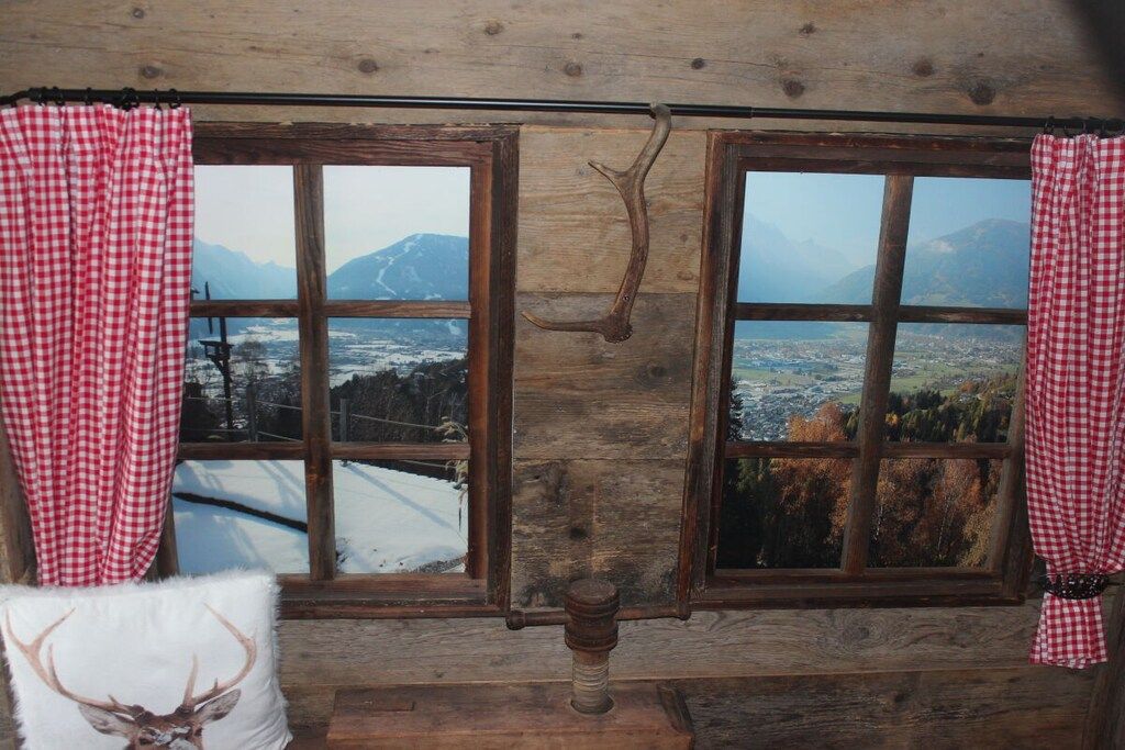 A room with two windows, wooden walls, and a view of a snowy landscape with mountains.
