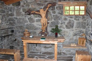 A wooden crucifix on a stone wall, a small table with a book, and a window with a view of greenery. - Panoramic view - East Tyrol (9991 Dölsach)