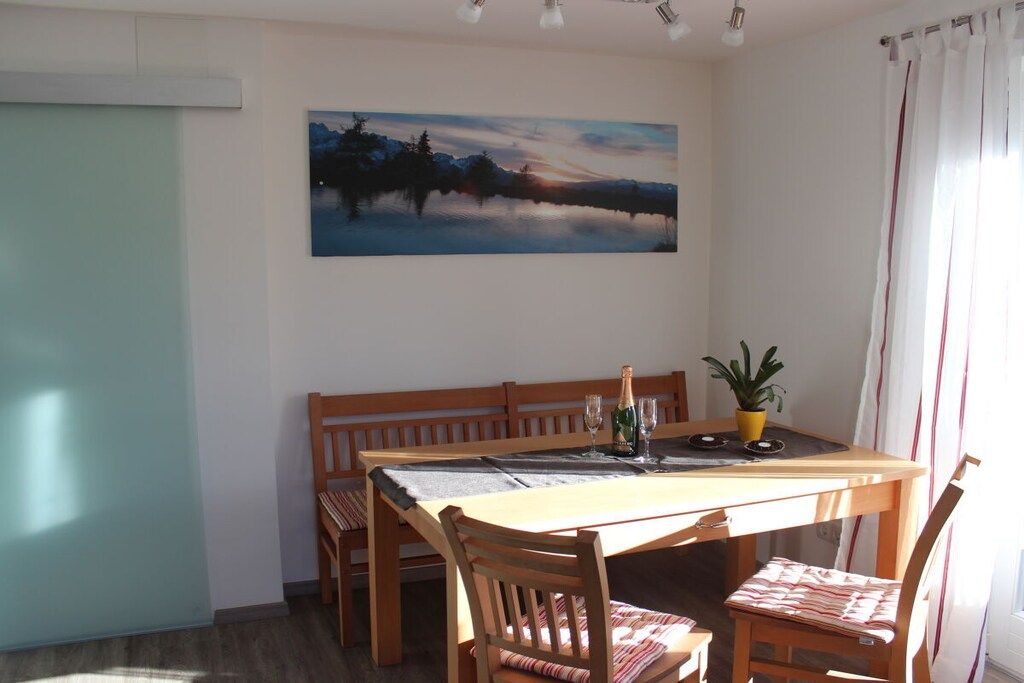 A dining area with a wooden table, chairs, a bench, a painting on the wall, and a potted plant.