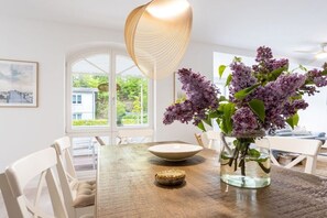 A dining area with a wooden table, white chairs, a vase with flowers, and a hanging light fixture. - Holiday apartment with 2 bedrooms (Ostseebad Binz)