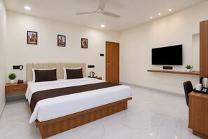 A modern hotel room with a large bed, a flat-screen TV, a desk, and a ceiling fan.