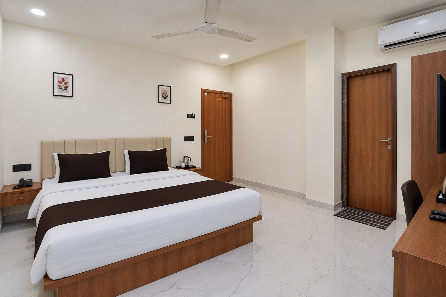 Habitación de hotel con cama, mesitas de noche, escritorio, silla, armario, ventilador de techo y aire acondicionado.