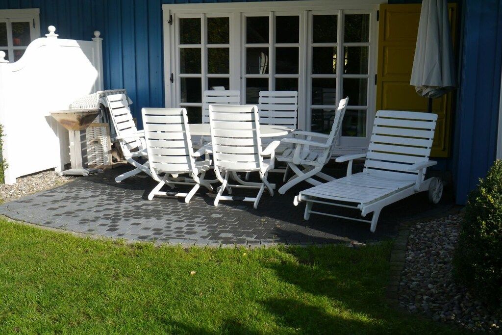 A patio with white lounge chairs and a table, a blue building, and a yellow door.