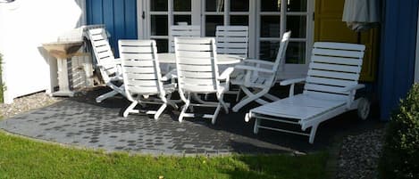 En terrasse med hvide loungesenge og et bord, en blå bygning og en gul dør.