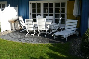 Een terras met witte lounge fauteuils en een tafel, een blauw gebouw en een gele deur.