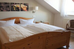 Ein Zimmer mit einem Einzelbett, einem Holzkopfende, weißer Bettwäsche, einem Nachttisch mit Lampe und einem Sessel.
