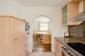 Una cocina con armarios de madera, un comedor con mesa y sillas, y una vista a través de un arco hacia otra habitación.