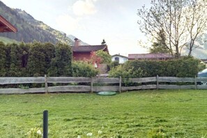 A fenced yard with a grassy area, a wooden fence, and a building with a red roof. - Holiday home in Rauris with swimming pool (Rauris)