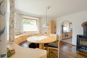 A cozy room with a round wooden table, a bench, a hanging light fixture, and a view of the kitchen through an archway. - Holiday home in Rauris with swimming pool (Rauris)