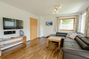 Una sala de estar con televisor de pantalla plana, muebles de madera, un sofá y una ventana con cortinas.