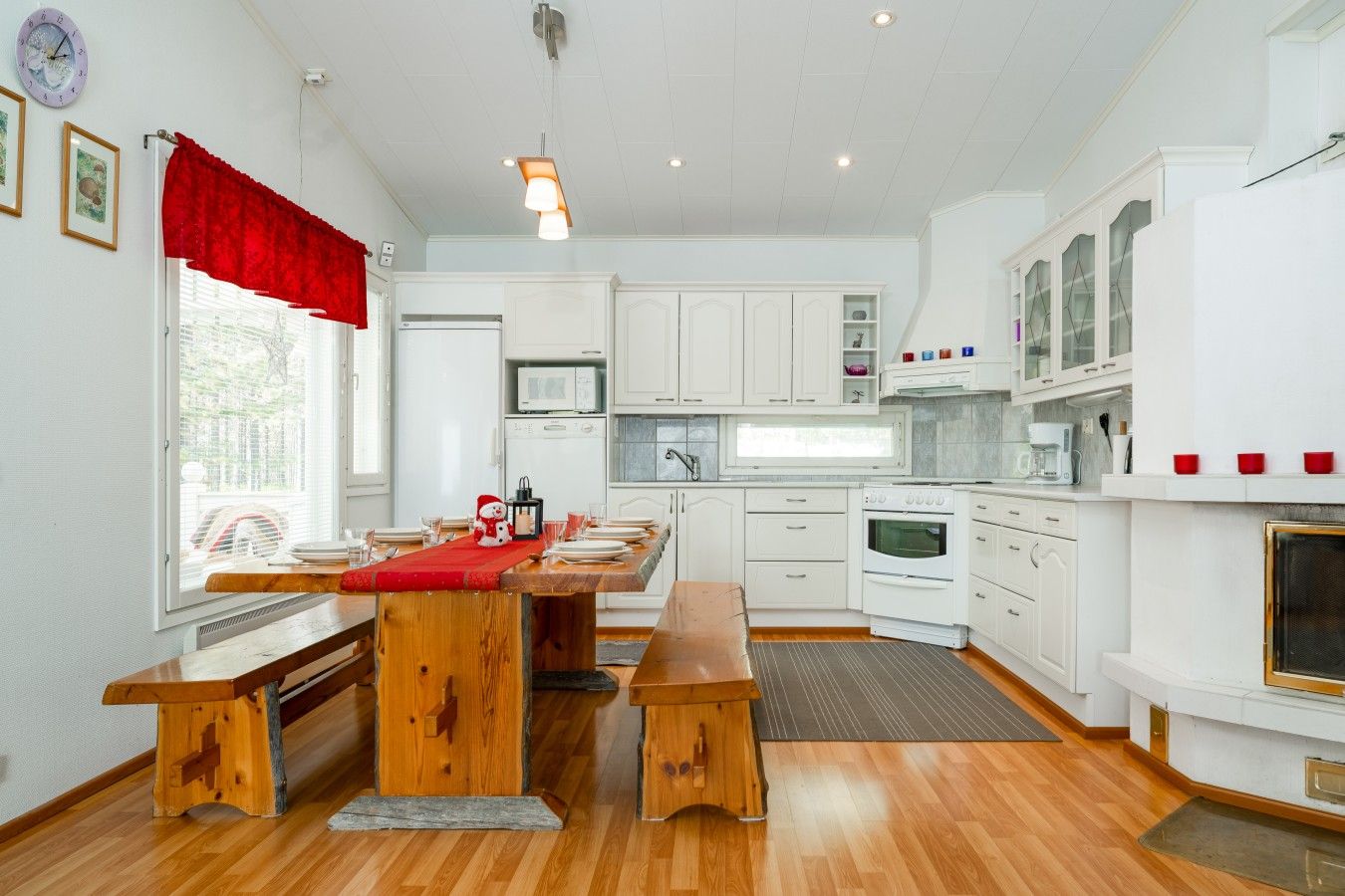 Une cuisine moderne avec des meubles blancs, une table à manger en bois et un rideau rouge.