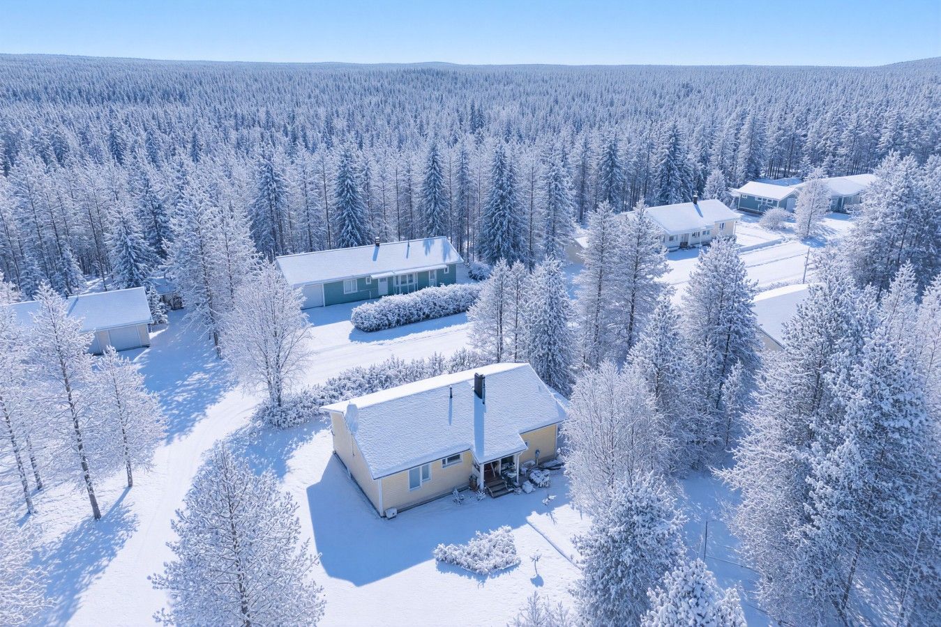A snow-covered landscape with multiple buildings, including a main house with a porch and a garage.