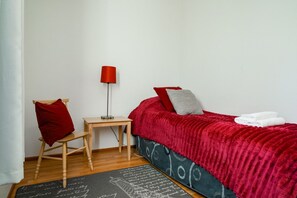 A bedroom with a bed, a chair, a small table, and a lamp.