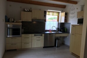 A compact kitchen with a built-in oven, dishwasher, and a window with curtains. - Holiday home in Kägsdorf with swimming pool (Kägsdorf)