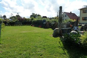 A grassy outdoor area with a wooden fence, a stone structure, and a house in the background. - Holiday home in Kägsdorf with swimming pool (Kägsdorf)