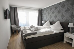A hotel room with a bed, a chair, a nightstand, and a TV. - Villa Louisa 40 - Lighthouse (Ostseebad Sellin)