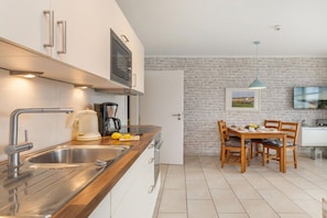 A modern kitchen with a wooden countertop, stainless steel sink, and a dining area with wooden chairs and a table. - Dune Residence Queen Augusta 5 (Ostseebad Binz)