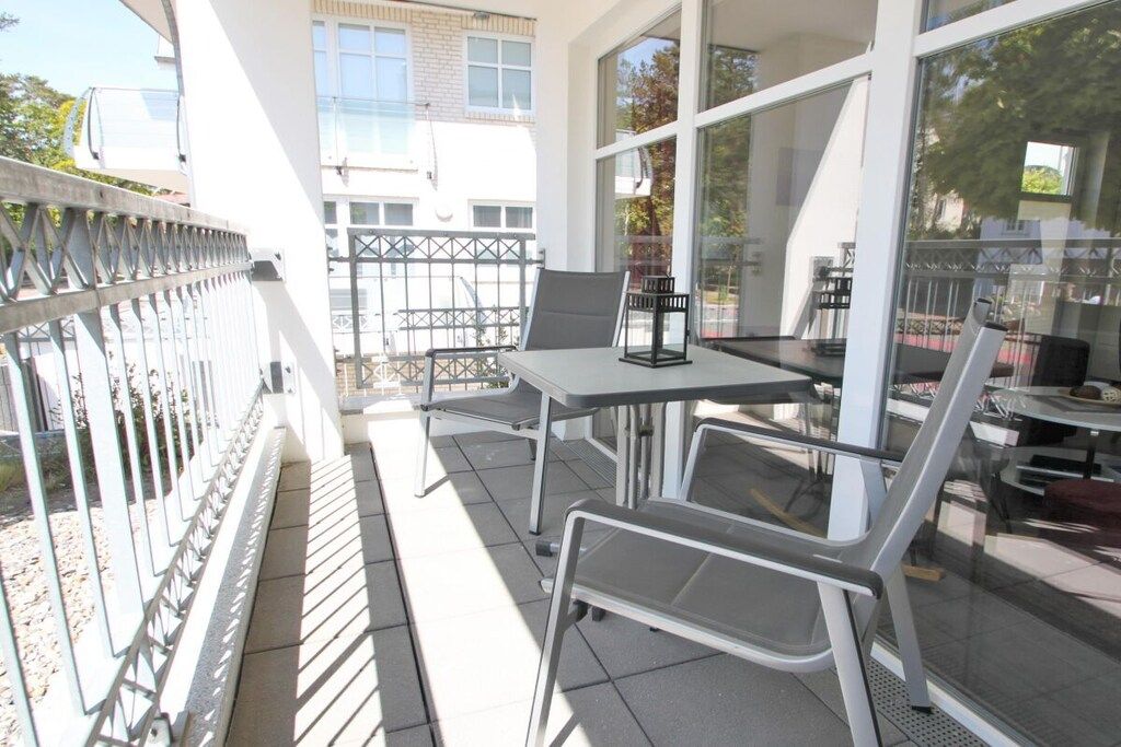 Ein Balkon mit Tisch und Stühlen, Geländer aus Glas und Blick auf Gebäude im Hintergrund.