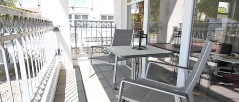 Un balcon avec une table et des chaises, une balustrade en verre et une vue sur les bâtiments en arrière-plan.