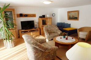 A living room with a television, two armchairs, a sofa, a small table with a lamp, and a large plant. - Apartment "Im Wiesengrund" (Kühlungsborn)