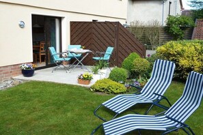 A patio with a table and chairs, a fenced garden area, and two striped lounge chairs. - Apartment "Im Wiesengrund" (Kühlungsborn)