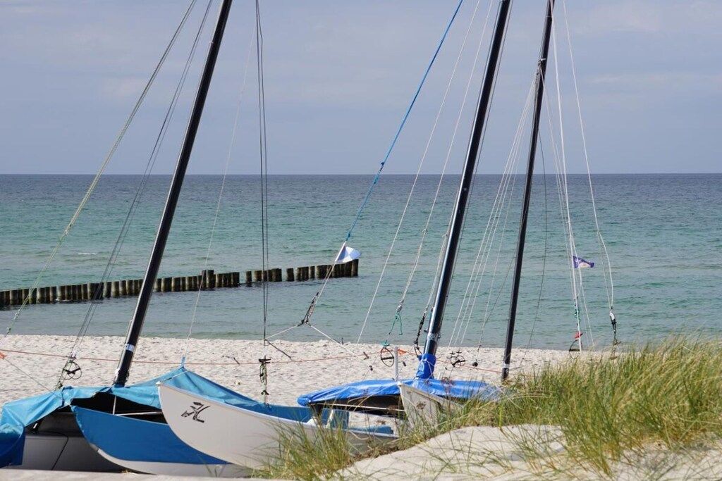 Ein Strand mit verankerten Segelbooten, einer Holzsteganlage und einem klaren Himmel.