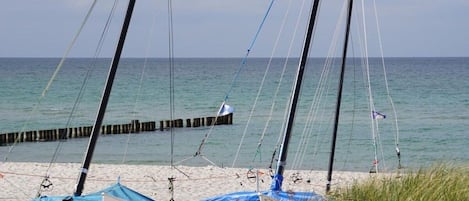 Ein Strand mit verankerten Segelbooten, einer Holzsteganlage und einem klaren Himmel.
