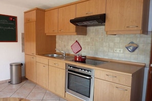 Una cocina con armarios de madera, un horno de acero inoxidable, un lavamanos y una olla roja sobre la encimera.