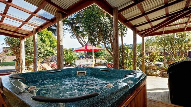 A hot tub with a wooden deck and a covered area with a red umbrella. - The Factory (Hapuku)