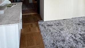Corredor estreito com uma porta branca à direita e um banheiro visível através de uma porta aberta à esquerda.