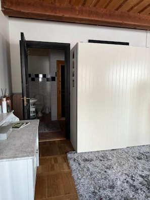 A narrow hallway with a white door on the right and a bathroom visible through an open door on the left.