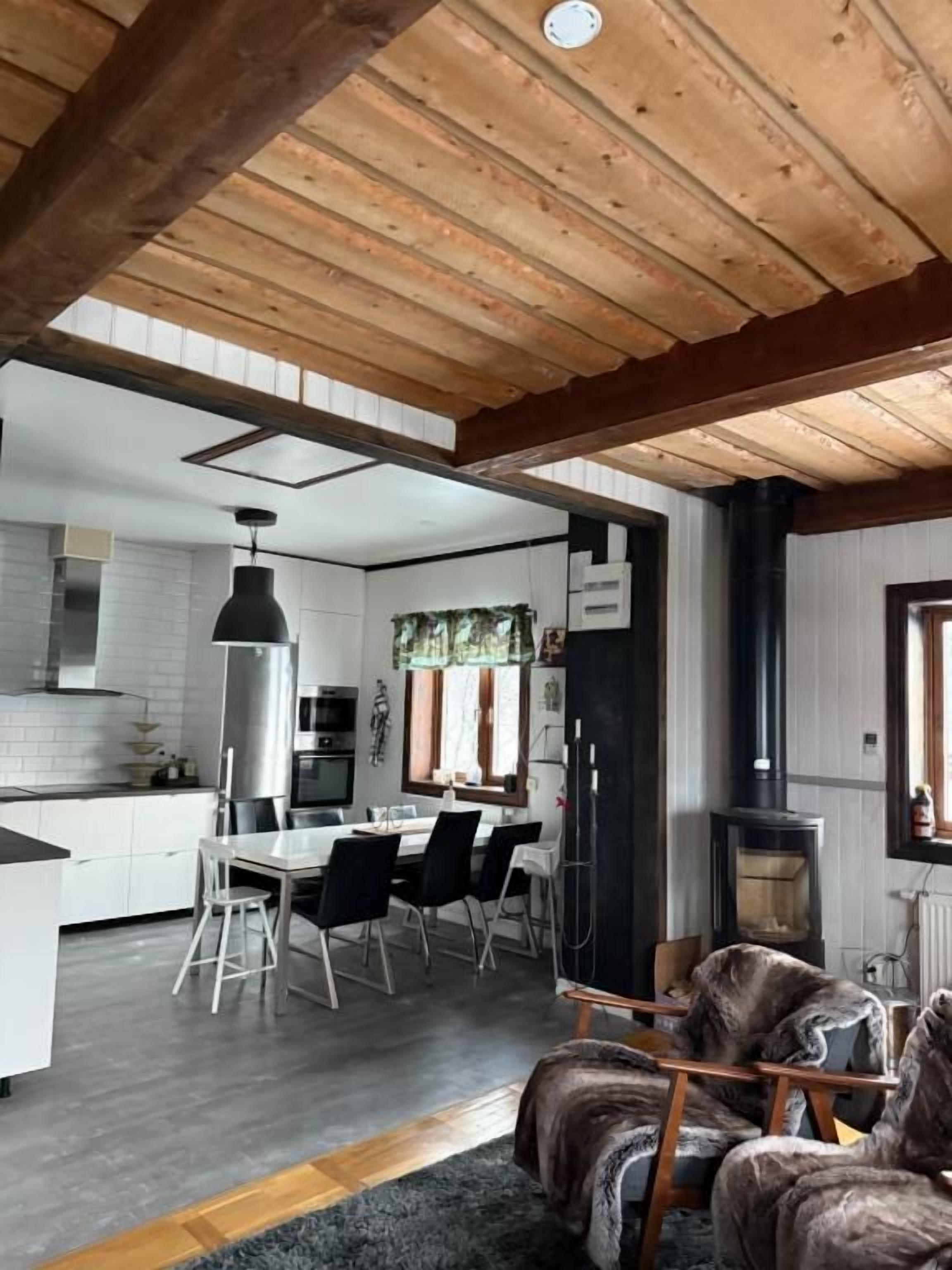 A modern kitchen with white cabinets, a dining area with a table and chairs, a black stove, and a wooden ceiling.