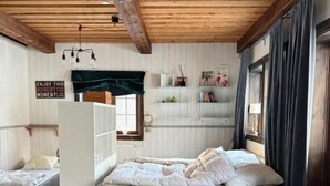 Quarto com cama, cadeira, tapete e prateleira com objetos.