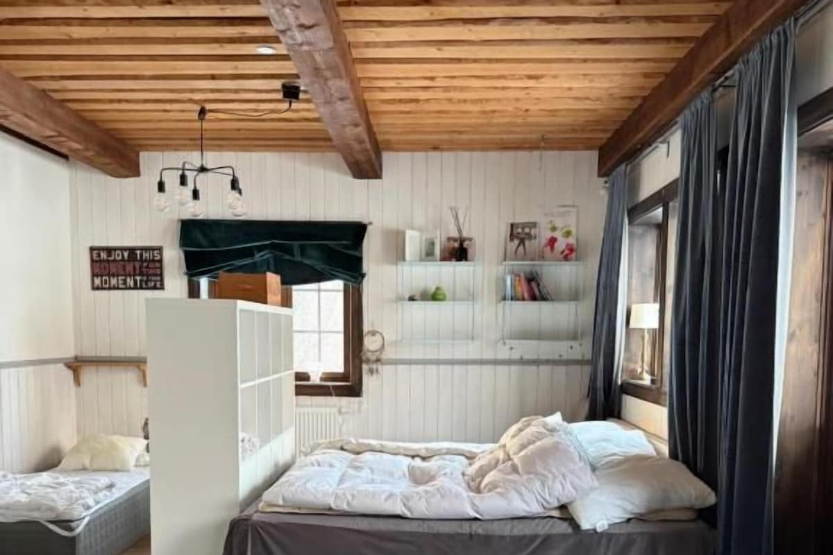 A bedroom with a bed, a chair, a rug, and a shelf with items.