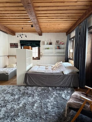 A bedroom with a bed, a chair, a rug, and a shelf with items.