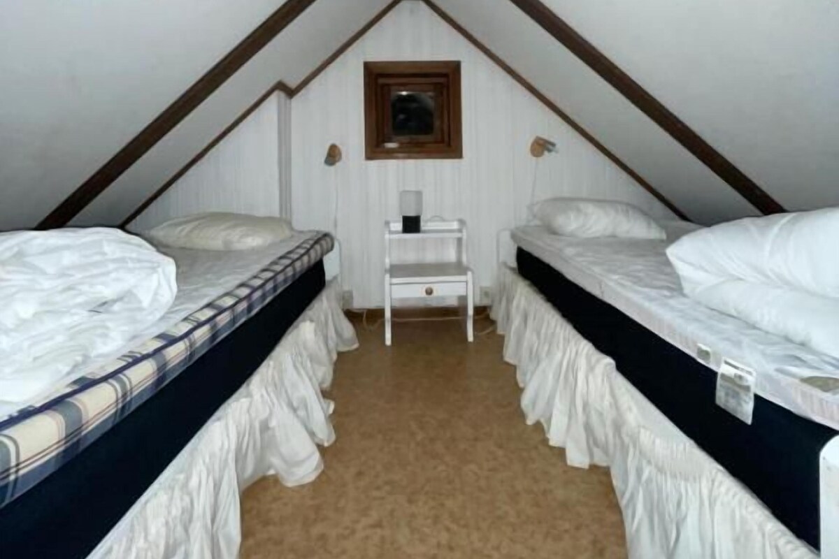 A small attic bedroom with two beds, a wooden ceiling, and a small window.