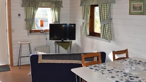Um quarto com televisão, uma mesa com toalha de mesa florida e um sofá.