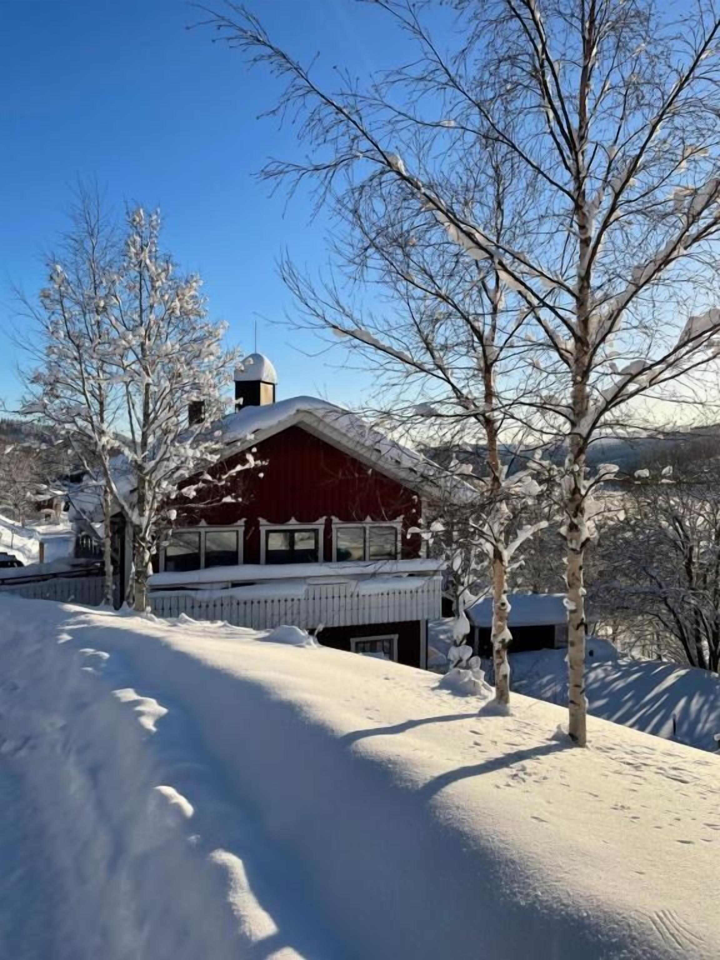 A snow-covered landscape with a red building featuring a balcony and a chimney.