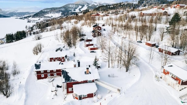 Vila coberta de neve com edifícios de telhados vermelhos, uma estrada sinuosa e uma montanha ao fundo.