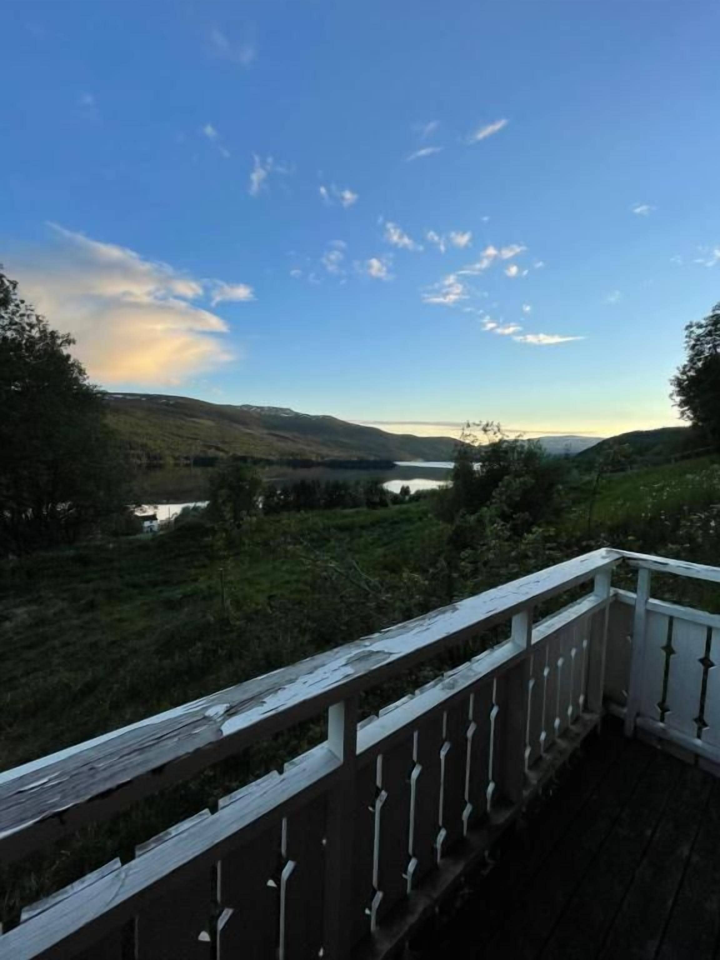 A wooden deck with a railing overlooking a lake and hills.