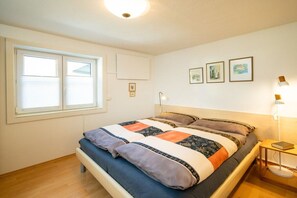Ein Schlafzimmer mit einem Bett, einem Nachttisch, einer Lampe und einem Fenster.