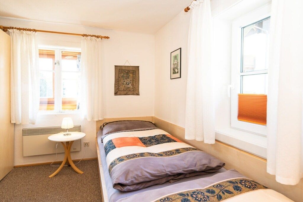 Un dormitorio pequeño y acogedor con una cama individual, una mesita de noche con lámpara, un radiador y una ventana con cortinas.