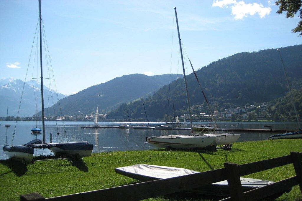 A lakeside view with boats docked along the shore, a wooden fence, and a backdrop of mountains.