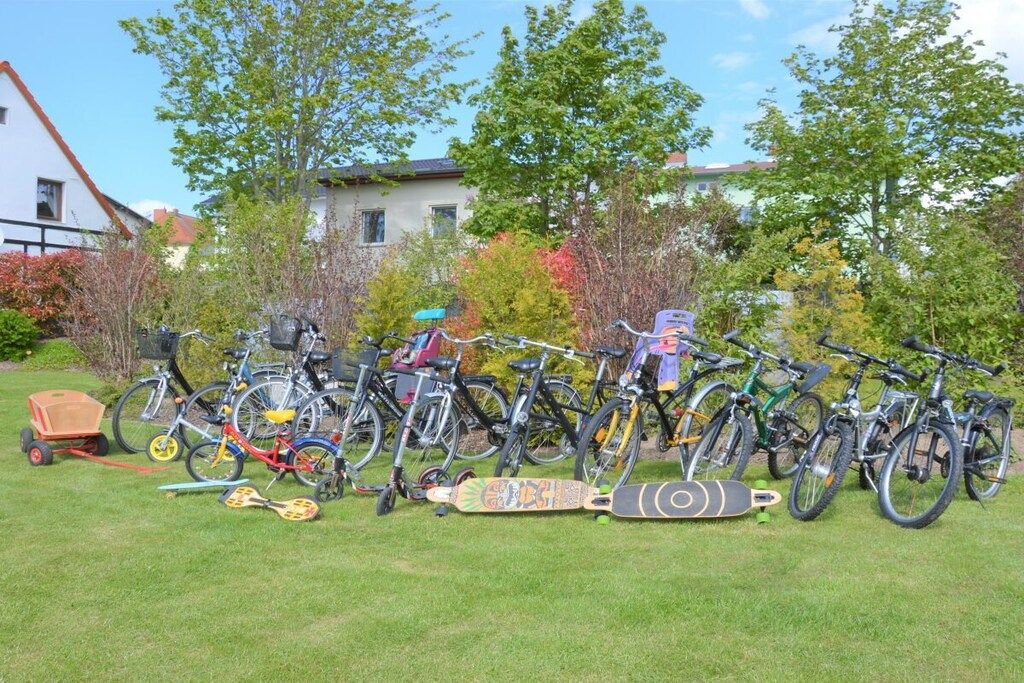 A row of bicycles and a skateboard in a grassy area with trees and a building in the background.