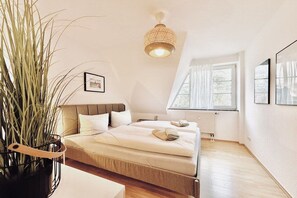 Ein Schlafzimmer mit einem Bett, einem Nachttisch, einer Topfpflanze, einer Pendelleuchte und einem Fenster mit Vorhängen.