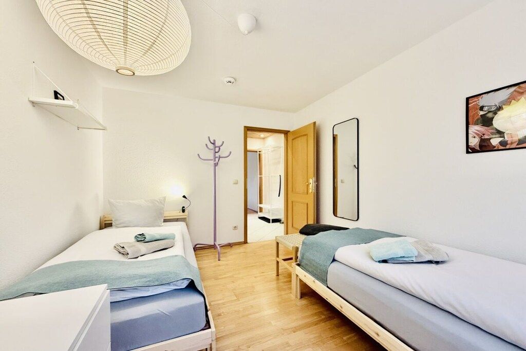 Ein modernes Schlafzimmer mit zwei Betten, einem Nachttisch, einer Lampe und einer Tür zu einem anderen Raum.