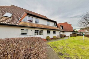 A two-story house with a tiled roof, a visible chimney, and a small garden area with a pathway leading to the entrance. - Holiday apartment with 2 bedrooms (Dierhagen)